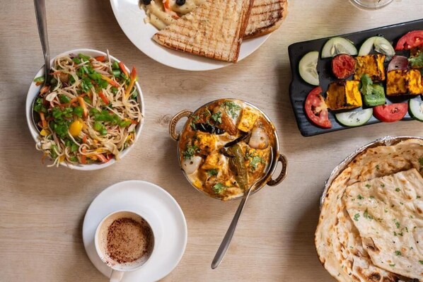 Une variété de plats, dont une salade, du paneer tikka et du pain naan, sont disposés sur une table en bois.