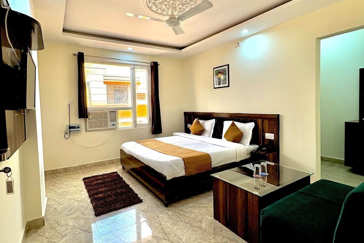 Habitación de hotel con cama, escritorio, silla, televisión y ventana con cortinas.