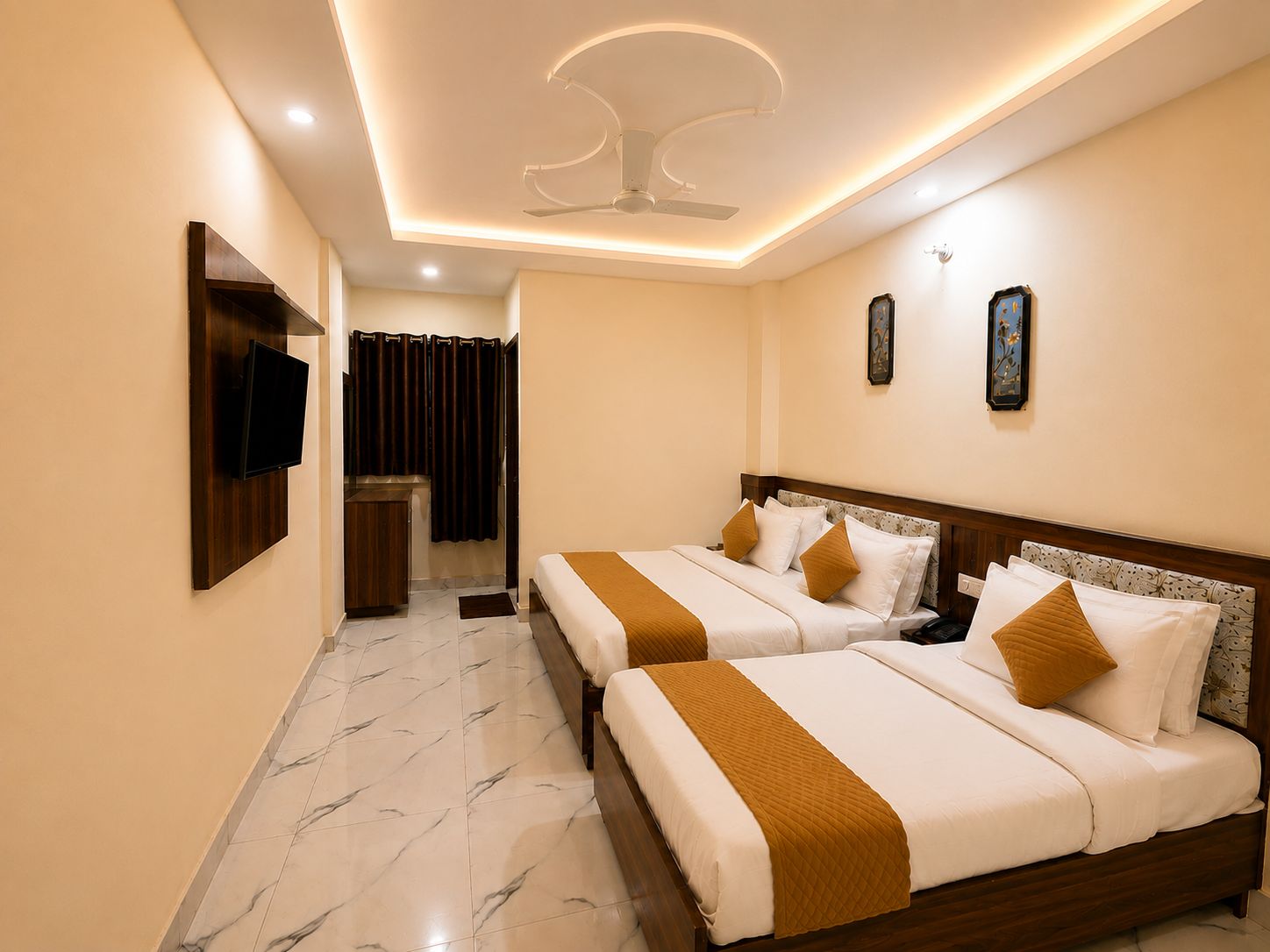 A hotel room with two beds, a TV mounted on the wall, a ceiling fan, and a small bathroom with a shower curtain.