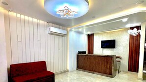 A modern reception area with a flat-screen TV, a wooden reception desk, and a red sofa. - Hotel Royal Central Haridwar (Haridwar)