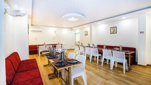 A dining area with multiple tables and chairs, a red sofa, and a ceiling light fixture. - Hotel Royal Central Haridwar (Haridwar)