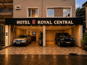 A hotel entrance with a sign reading 'HOTEL ROYAL CENTRAL,' two SUVs parked in the driveway, and a television screen on the wall.