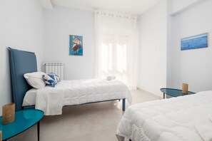 A bedroom with two beds, a blue headboard, a small table, and a painting on the wall. - Surya | Elegant Apartment with Balcony in the Heart of Sorrento (Sorrento)