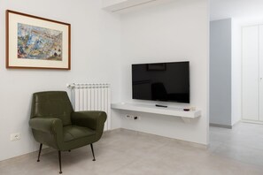 A modern living room with a flat-screen TV on a white wall, a green armchair, and a framed artwork above the TV. - Surya | Elegant Apartment with Balcony in the Heart of Sorrento (Sorrento)