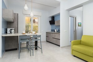 A modern kitchen with a dining area, a sofa, and a view of the outdoors.