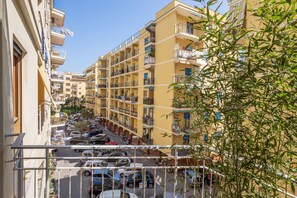 A multi-story residential building with balconies, a parking area in front, and a clear sky.