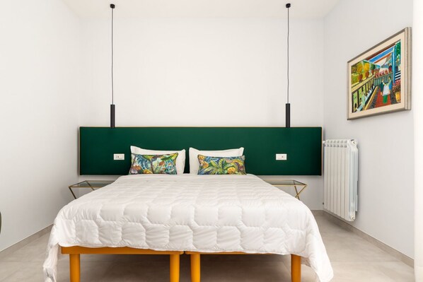 A bedroom with a bed, a green headboard, a radiator, and a painting on the wall.
