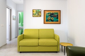 Een moderne woonkamer met een bank, een klein rond tafeltje en twee ingelijste kunstwerken aan de muur.