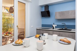 A modern kitchen with a dining area, featuring a coffee machine, cups, and pastries on the table. - Surya | Elegant Apartment with Balcony in the Heart of Sorrento (Sorrento)