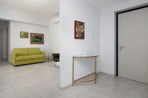 A modern living room with a yellow sofa, a glass-top coffee table, and two framed artworks on the wall.