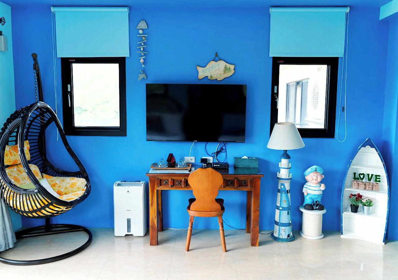 A room with a blue wall, a wooden desk, a television, a hanging chair, a small statue, and a white shelf with the word "LOVE".