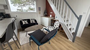 Un espace de vie moderne comprenant un coin repas, un canapé agrémenté de coussins décoratifs, une table basse, un fauteuil et un escalier.