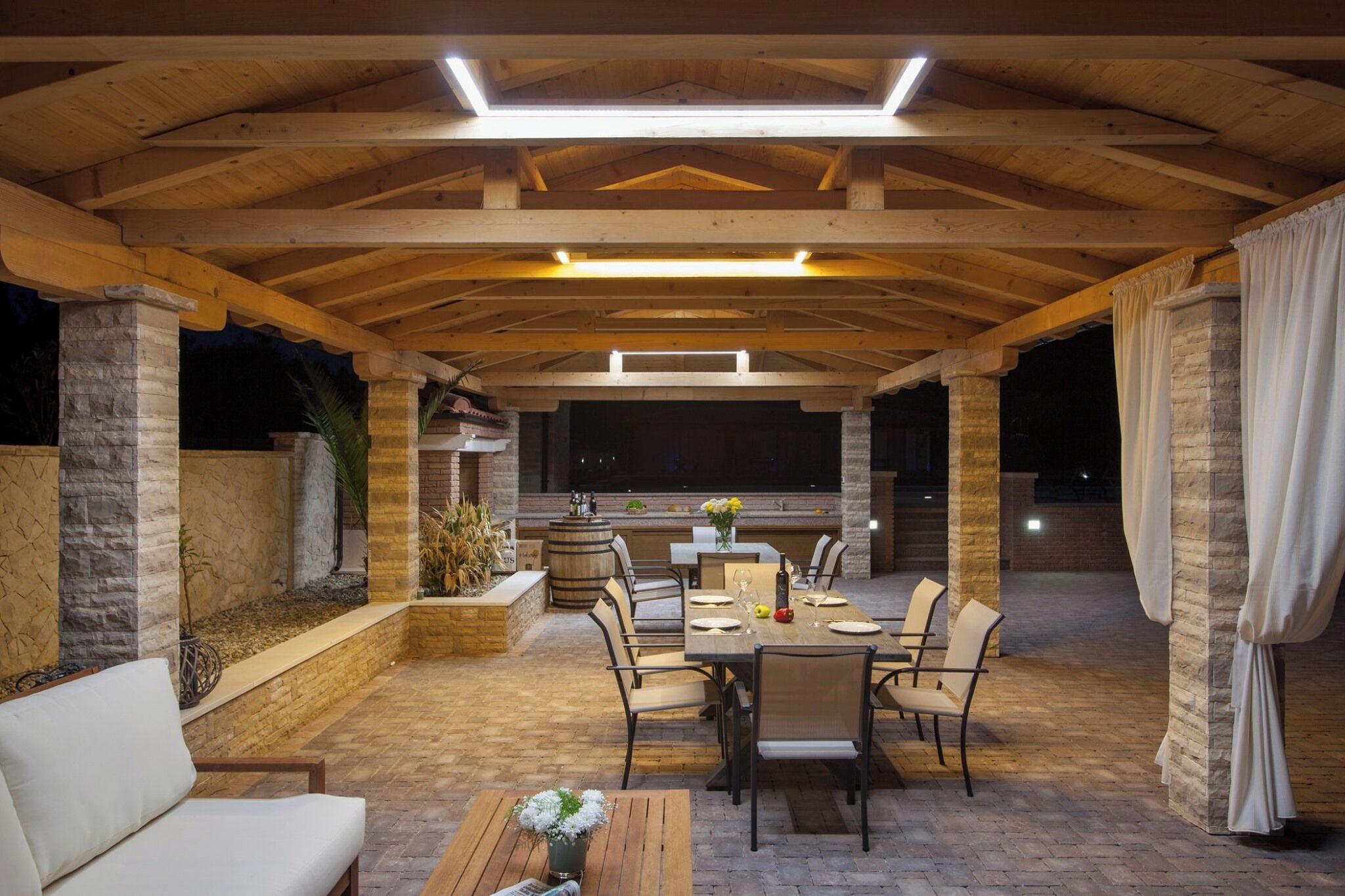 An outdoor patio area with a wooden ceiling, stone pillars, and a dining table set for four.