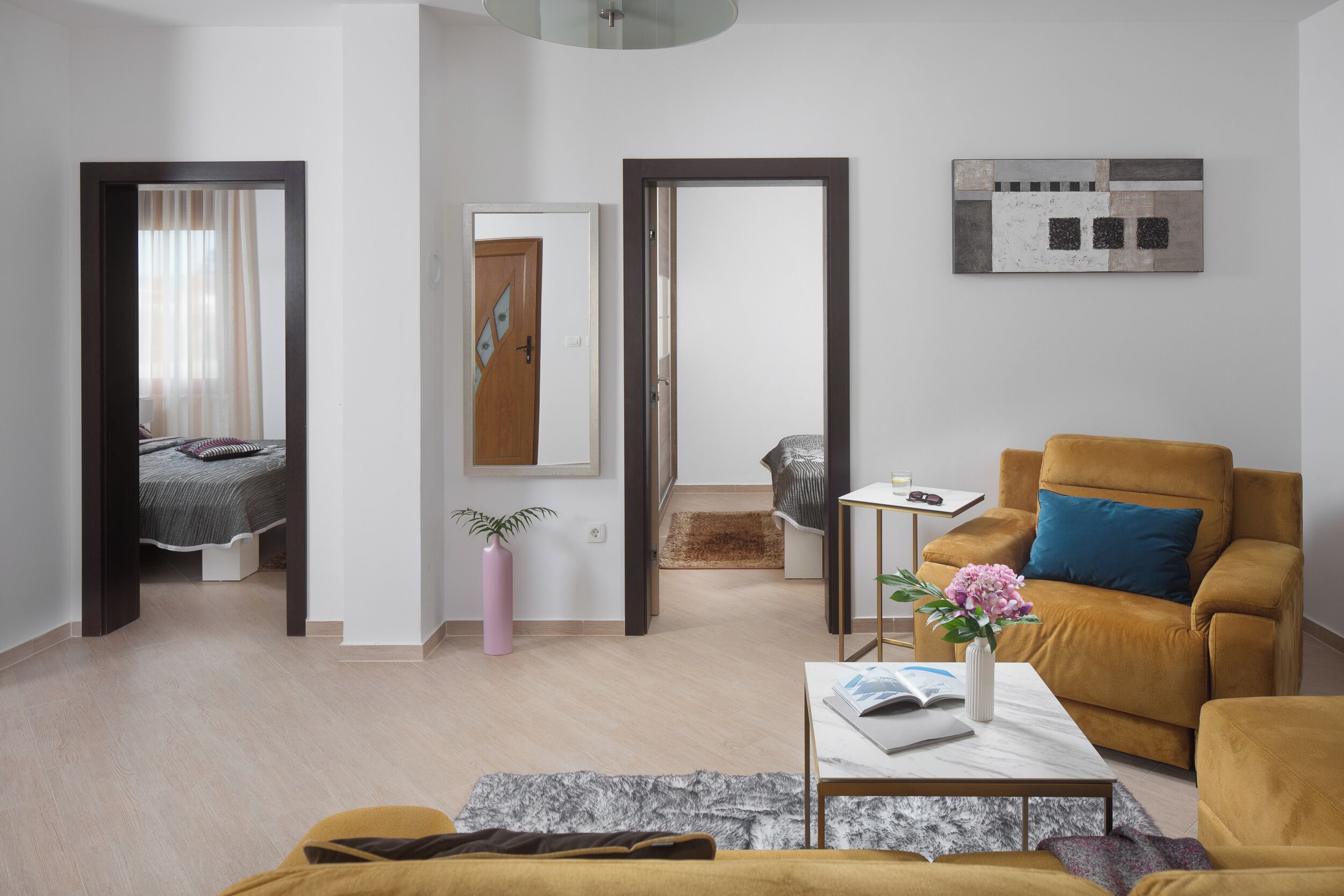 A modern living room with a sofa, a coffee table with a book and vase, a bed with a curtain, and a painting on the wall.