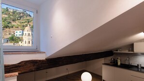 A kitchen with a wooden beam ceiling, a view of a town through a window, and a round light fixture. - VERNAZZA - ANGEINETTA, elegant suite-loft with every comfort (vernazza)