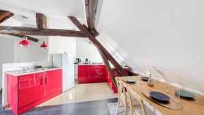 A modern kitchen with red cabinetry, a wooden dining table, and exposed wooden beams. - Drouais Night (Dreux)