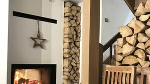 A cozy interior with a fireplace, a wooden chair, and a staircase with stacked firewood. - Villa in Tanvald Near Ski Slopes (Tanvald)