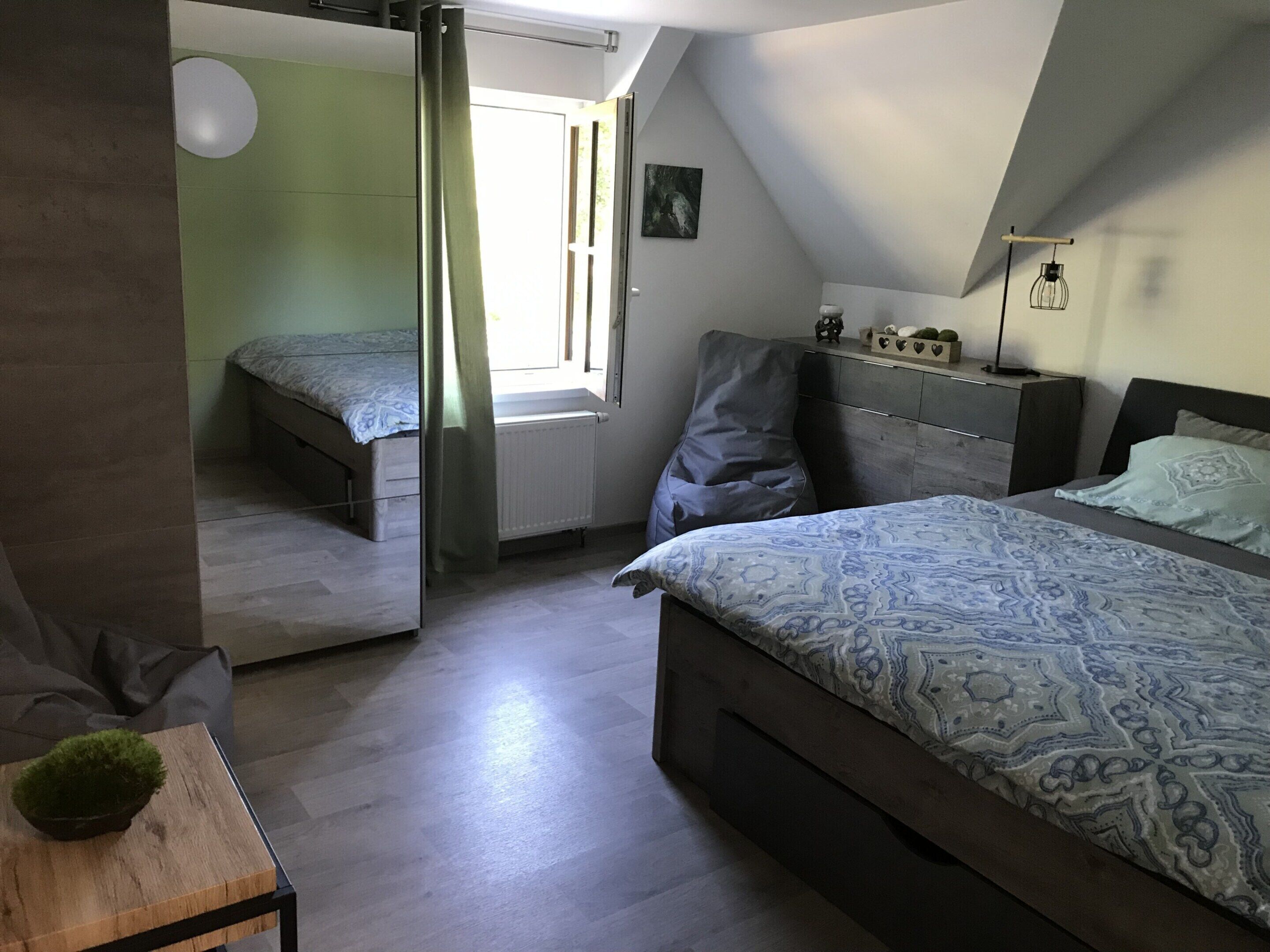 Ein Schlafzimmer mit zwei Betten, einem Fenster, einer Heizung, einem Nachttisch und einer Wandleuchte.