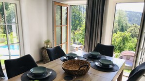 A dining table set with black plates, bowls, and a woven basket, surrounded by chairs, with a view of greenery and a pool outside. - Villa in Tanvald Near Ski Slopes (Tanvald)