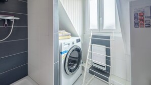 A compact laundry room with a washing machine, a drying rack, and a window providing natural light.