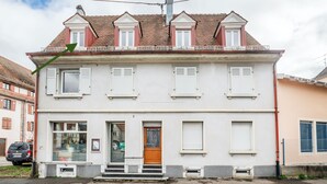 A two-story building with a white facade, a wooden door, and a balcony with a railing.