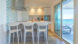 Una cocina moderna con una isla central, taburetes blancos y vistas al mar a través de amplios ventanales.
