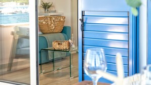 Una habitación con una puerta de vidrio que da a un balcón, un sofá color turquesa, una cesta de mimbre y una copa de vino sobre una mesa de madera.
