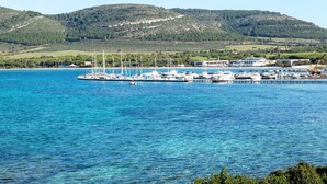 Un puerto deportivo con barcos amarrados, un muelle que se adentra en el agua y un paisaje montañoso al fondo.