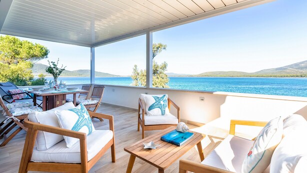 Un área de estar al aire libre techada, con muebles de madera, una mesa y vista al mar.