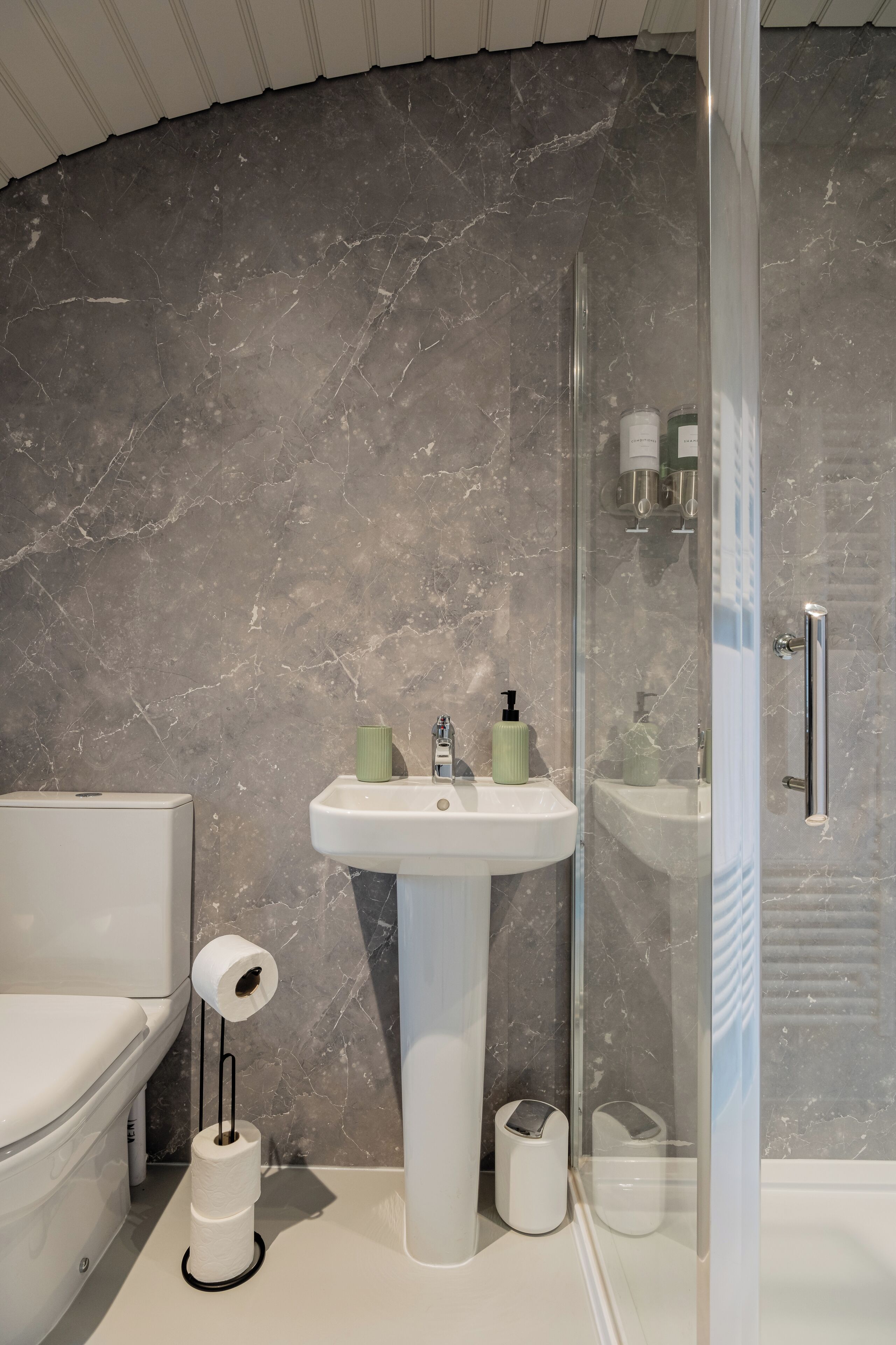 Un bagno moderno con parete in marmo, lavandino bianco e box doccia in vetro.