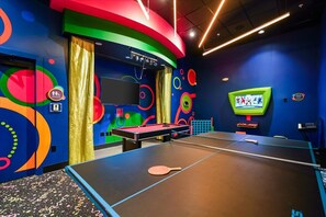 Una habitación con mesa de ping pong, mesa de billar y una pantalla de televisión.