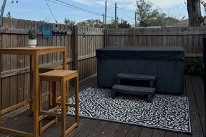 A wooden deck with a hot tub, a table, and a patterned rug.