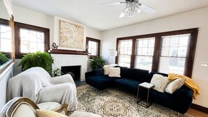 Un salon avec une cheminée, un canapé bleu foncé, un fauteuil blanc et un tapis à motifs.