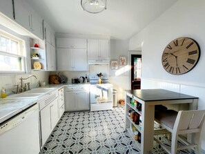 A kitchen with white cabinets, a patterned floor, a wooden clock, and a dining area with a table and chairs.