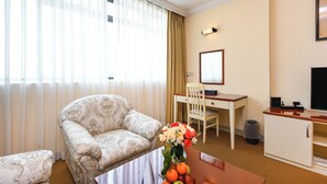 A hotel room with a sofa, a dining table with a vase of flowers, a desk with a chair, a television, and a cabinet. -  Cityview Serviced Apartment & Hotel Ho Chi Minh (Ho Chi Minh City)