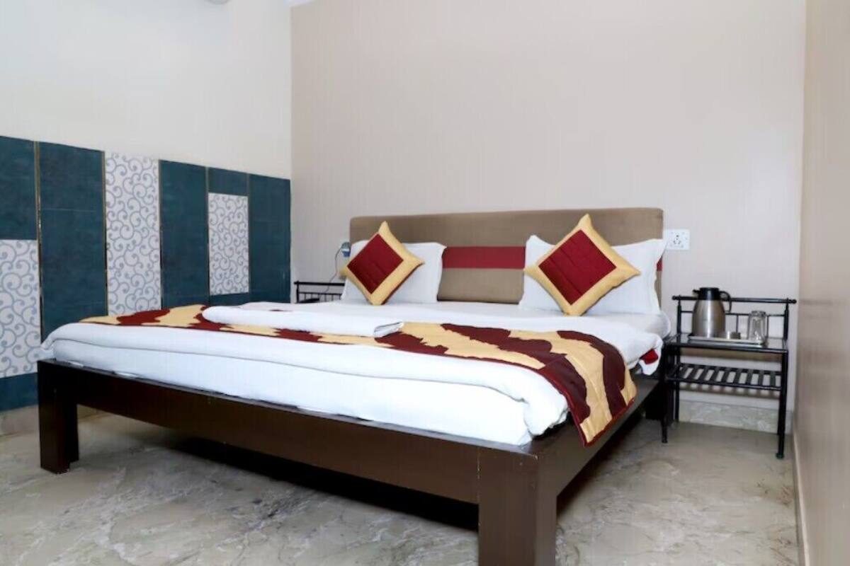 A neatly made bed with a patterned headboard, a bedside table with a kettle, and a wall with decorative tiles.