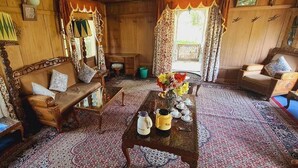 A traditional wooden room with a sofa, a table with tea sets, and patterned rugs. - Queens Lake House (Srinagar)