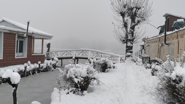 A wooden building with a snow-covered roof and a bridge in the background. - Queens Lake House (Srinagar)