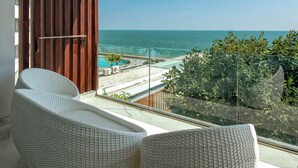 Un balcón con sillones de mimbre, vista al océano y una playa con piscina.