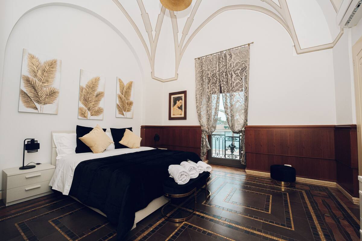 Ein Schlafzimmer mit einem großen Bett, einem Nachttisch, einer Kommode und einem Fenster mit Vorhängen.