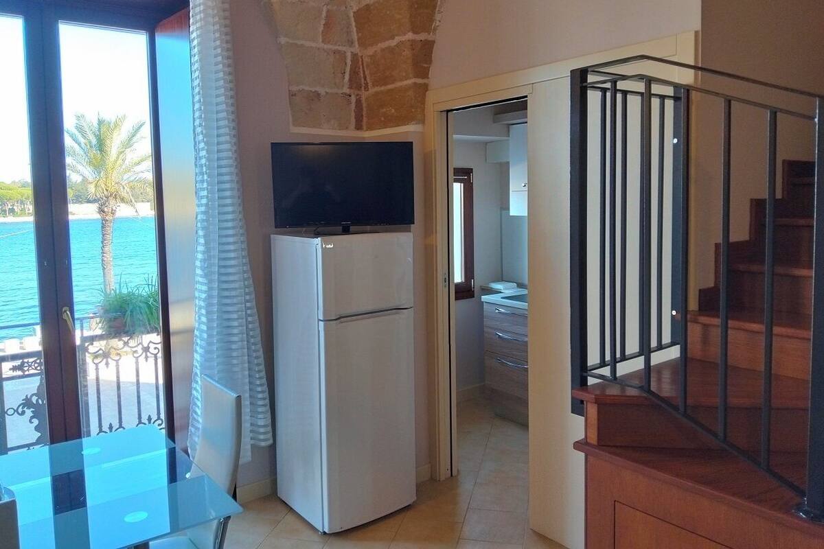 Eine kompakte Küche mit einem Kühlschrank, einem Flachbildfernseher und Meerblick durch eine Balkontür.