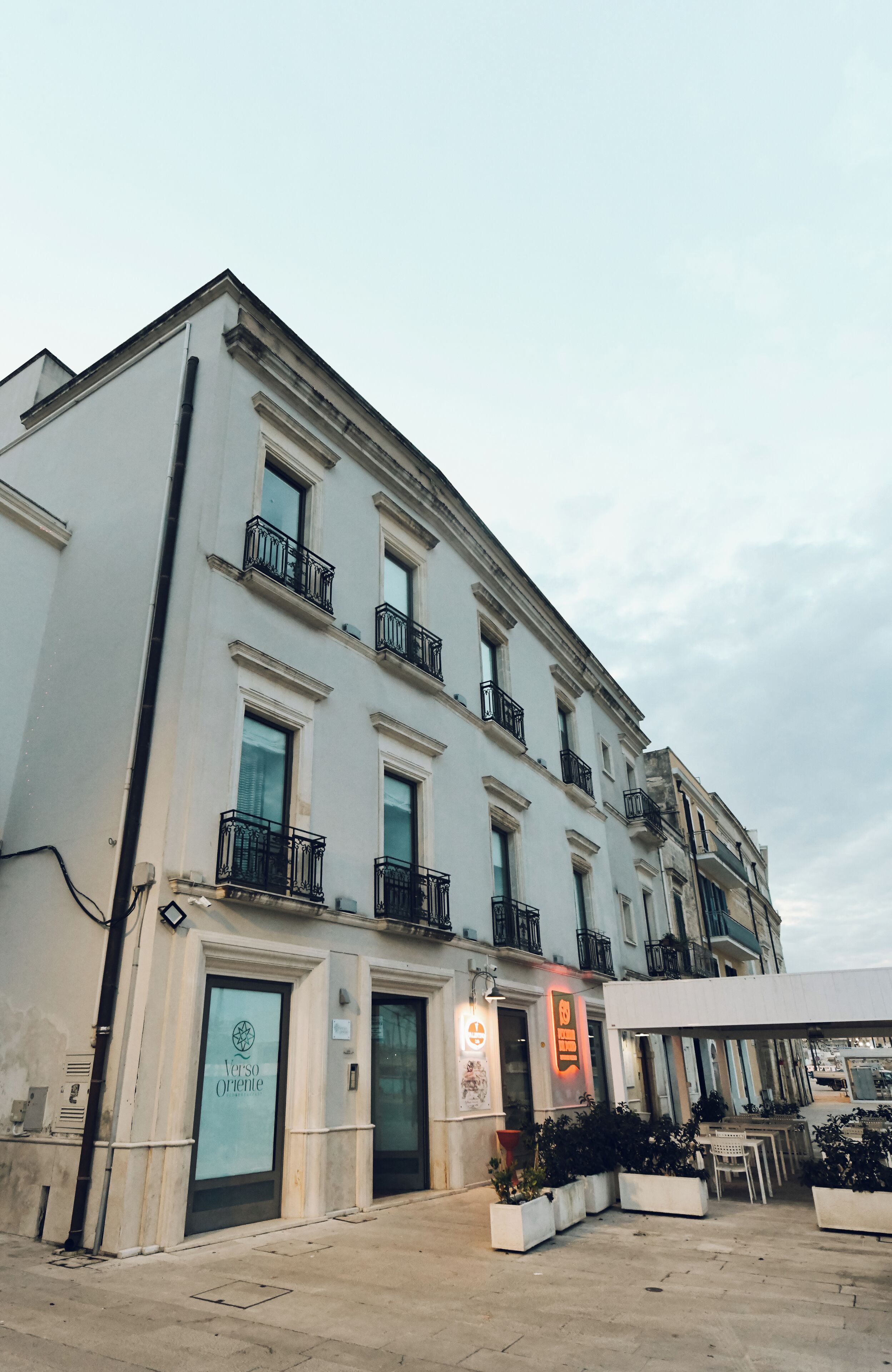 Un immeuble à plusieurs étages, de style architectural classique, avec une entrée au niveau du sol dotée d’une porte en verre et d’une enseigne indiquant « Verso Oriente ».