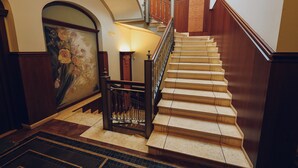 A grand staircase with a handrail, a painting on the wall, and a patterned floor. - Verso Oriente  (Brindisi)