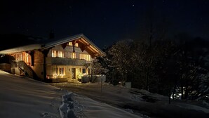 Een besneeerd landschap met een houten huis, verlicht door warme lichtjes.