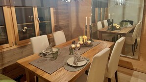 Een eetgedeelte met een houten tafel voor vier personen, omringd door stoelen. Er staan kaarsen en een decoratief middelpunt op de tafel.