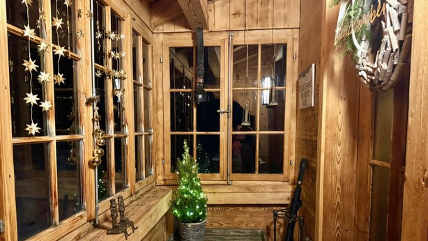 Een gezellig houten interieur met grote ramen, een kleine kerstboom en rustieke decoratie.