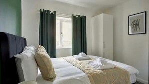 A hotel room with a bed, a bedside table, a window with curtains, a wardrobe, and a framed picture on the wall.