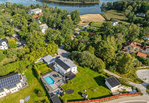 Ett flygbildsfoto av ett bostadsområde med hus, en swimmingpool och en stor byggnad med solpaneler.