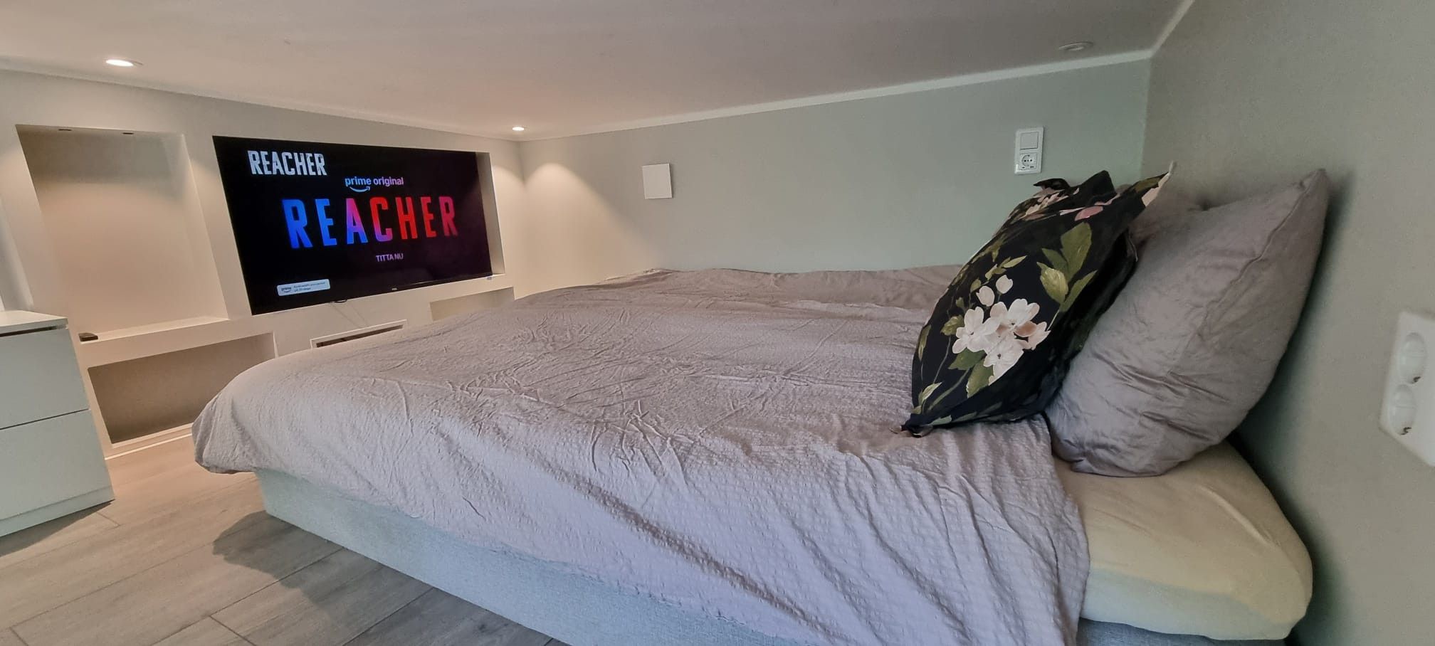 Een slaapkamer met een bed, een aan de muur bevestigde televisie en een nachtkastje.