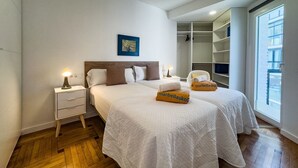 Une chambre d’hôtel avec deux lits, une table de chevet, un ventilateur de plafond, une grande fenêtre et un placard.
